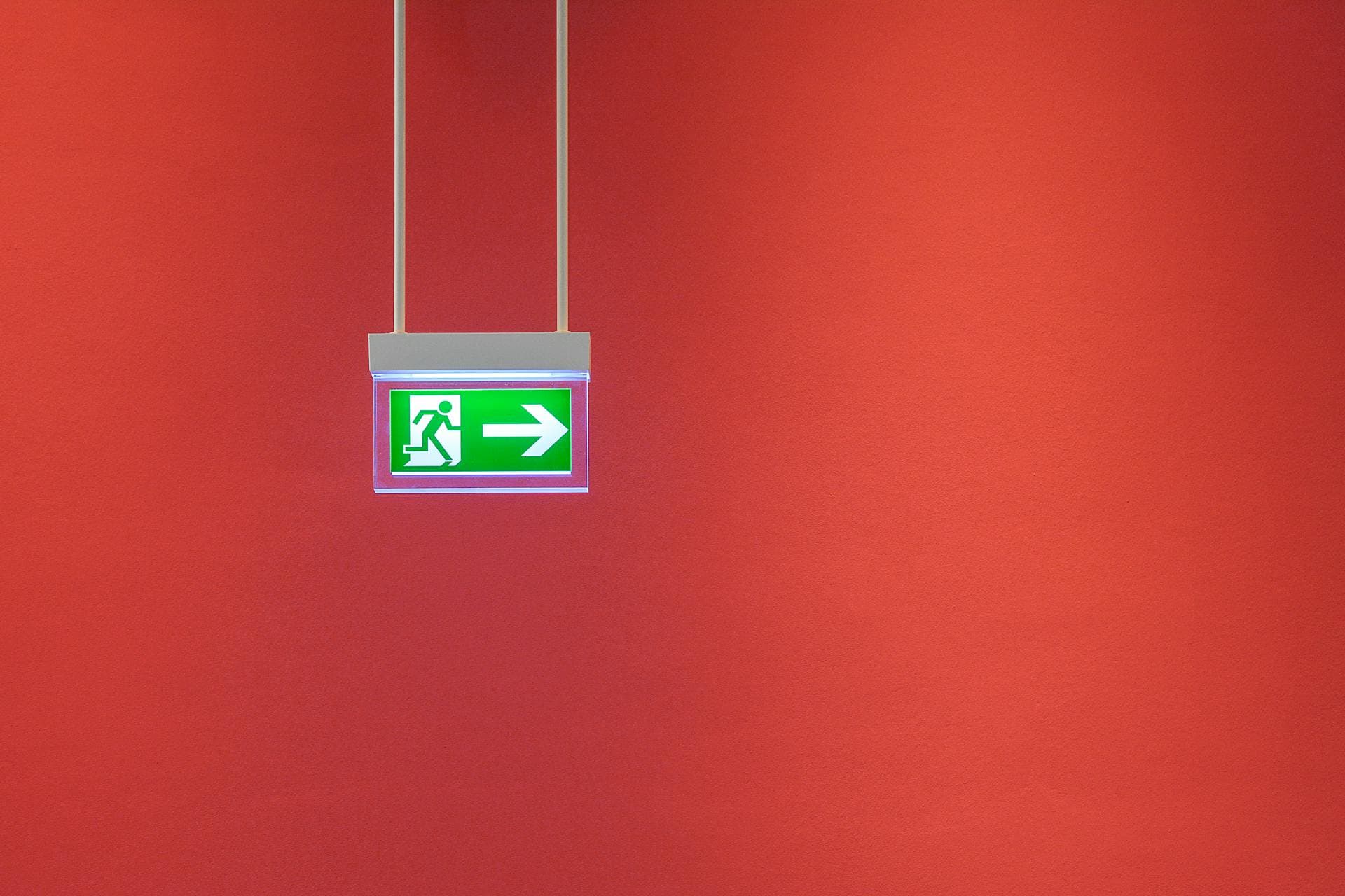 Green emergency exit sign hanging from a red wall